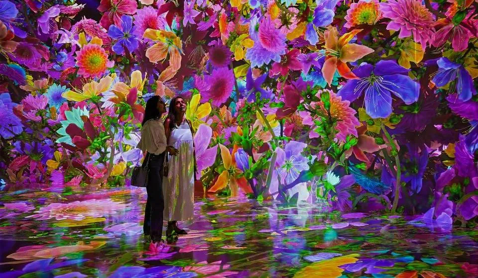 Visitantes recorren Blooming Wonders Houston en ARTECHOUSE, jardín digital interactivo con mariposas y flores tecnológicas.