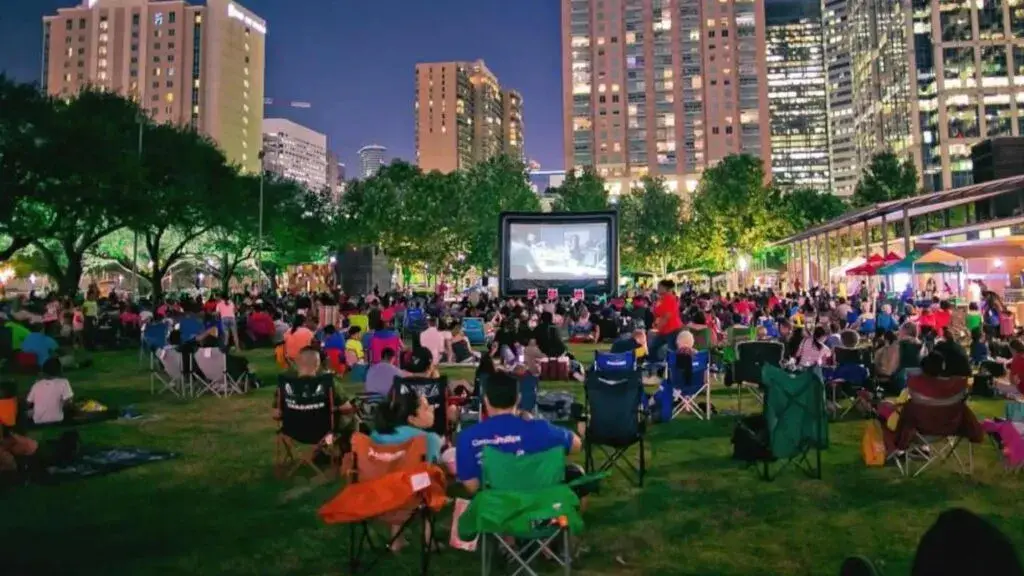 familias disfrutando cine al aire libre en parque con pantalla gigante y ambiente nocturno de verano