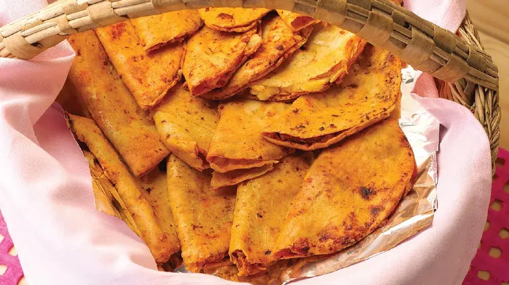 Una canasta tradicional con tacos sudados, tortillas brillantes y salsas mexicanas, en una escena de comida callejera.